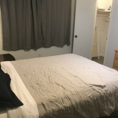 apartment bedroom with grey bed and grey curtains with closet door open