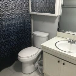 small white apartment bathroom with black and gray shower curtain, mirrored medicine cabinet, and white sink.