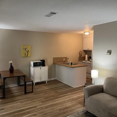 interior of apartment including a table with two benches, storage area with microwave, small kitchen, and couch with lamp