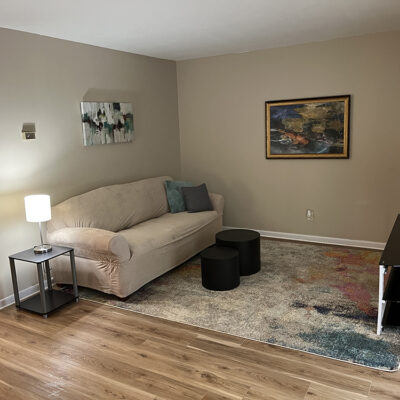 clean apartment living room with art on the walls, a beige sofa with pillows, rug, tv, tv stand, lamp, and end table